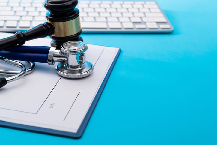 A gavel sitting over a stethoscope on top of a clipboard next to a keyboard.