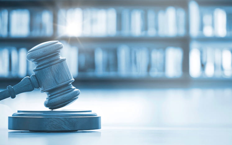 A photo of a wooden gavel in front of a bookshelf with a blue hue over it.