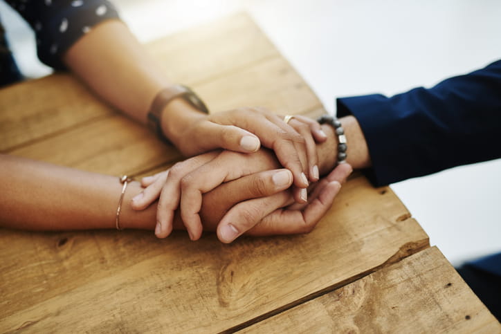 Two people holding hands as one person comforts the others.