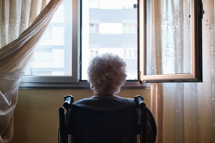 An older woman in a wheelchair staring out the window alone in a nursing home.