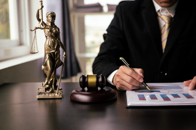 A Colorado pedestrian accident lawyer working on paperwork at his desk with the Lady Justice and a gavel next to him.