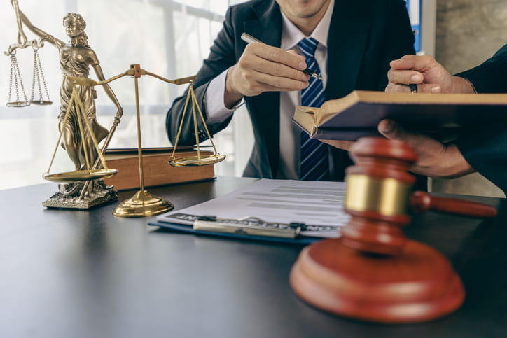 A Colorado sexual assault lawyer is reviewing a case with his coworker. In front of them is a gavel, paperwork, the scales of justice, a Lady Justice statue and a book. 