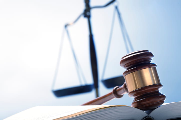 A gavel sitting on top of an open book with the scales of justice behind it. 